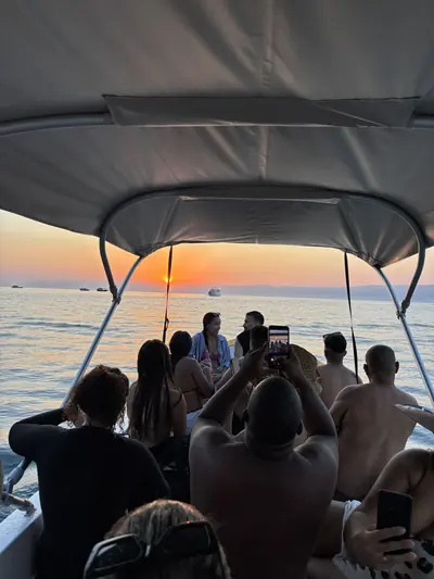 Grupo sentado no barco, de costas, vendo o sol nascer.