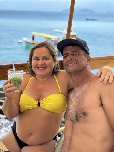 Casal a bordo com uma bebida na mão, o mar ao fundo.