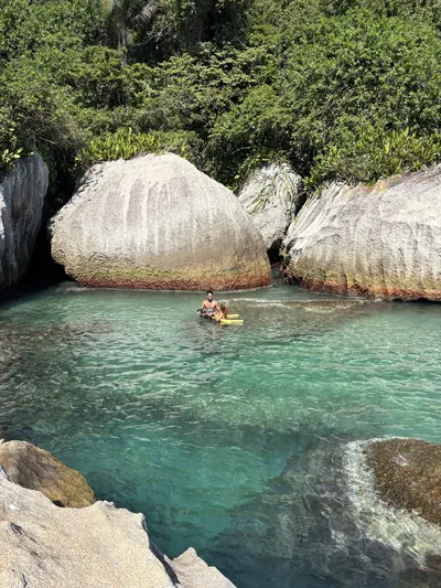 Pessoa boiando dentro de uma piscina natural entre pedras.