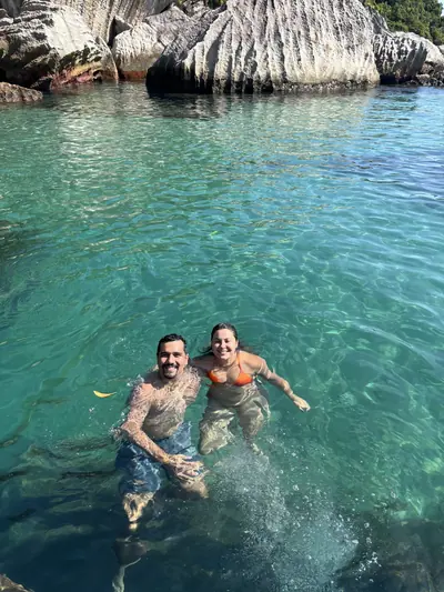 Casal na água rasa e transparente, junto às pedras.