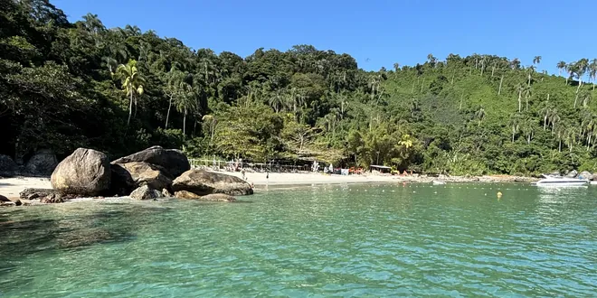 Praia de areia clara com quiosques e barcos ancorados na água rasa.